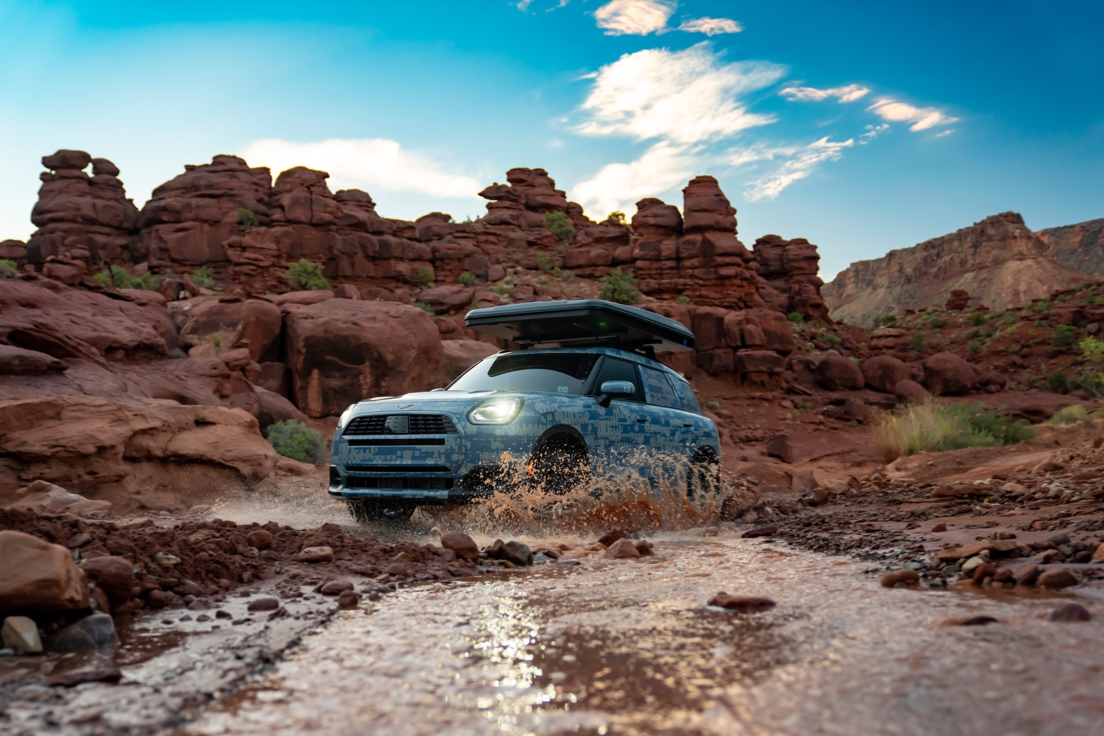 MINI Countryman a atravessar um riacho numa paisagem rochosa, com salpicos de  água e uma caixa de tejadilho 